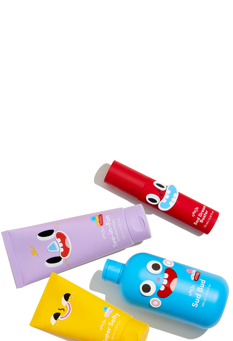Four colorful skincare product containers, each with a playful cartoon face design, are arranged on a white background. The bottles are yellow, purple, red, and blue.