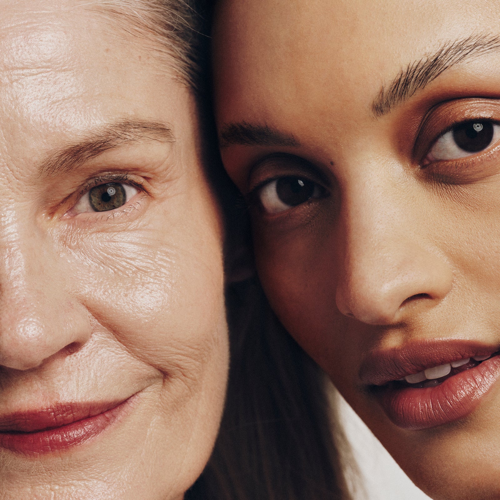 Close-up of two women’s faces, one older with light skin and gray hair, the other younger with medium skin and dark hair, both looking directly at the camera and smiling softly.