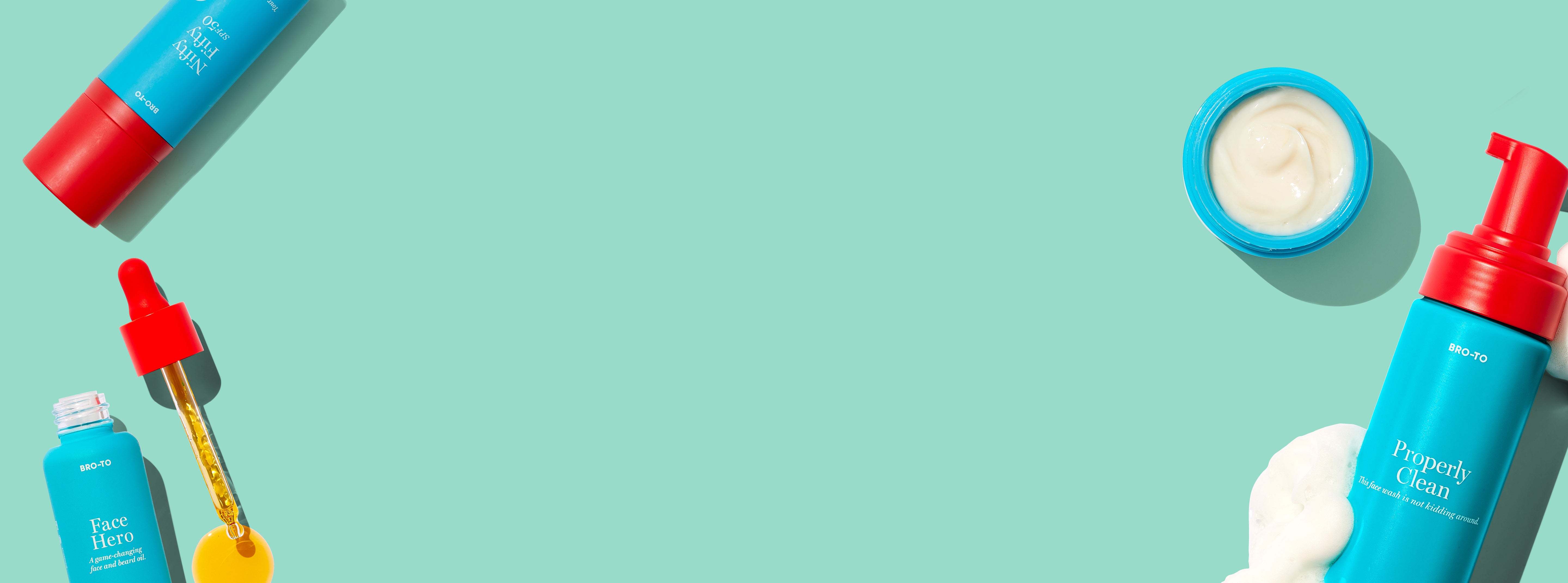 Flat lay of colorful skincare products including a serum with a dropper, a cream jar, and a foaming cleanser with some foam, arranged around the edges of a light turquoise background with empty space in the center.