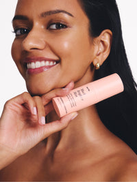 Smiling woman holds a pink skincare bottle labeled "brighter skin," showcasing glowing complexion and gold earrings