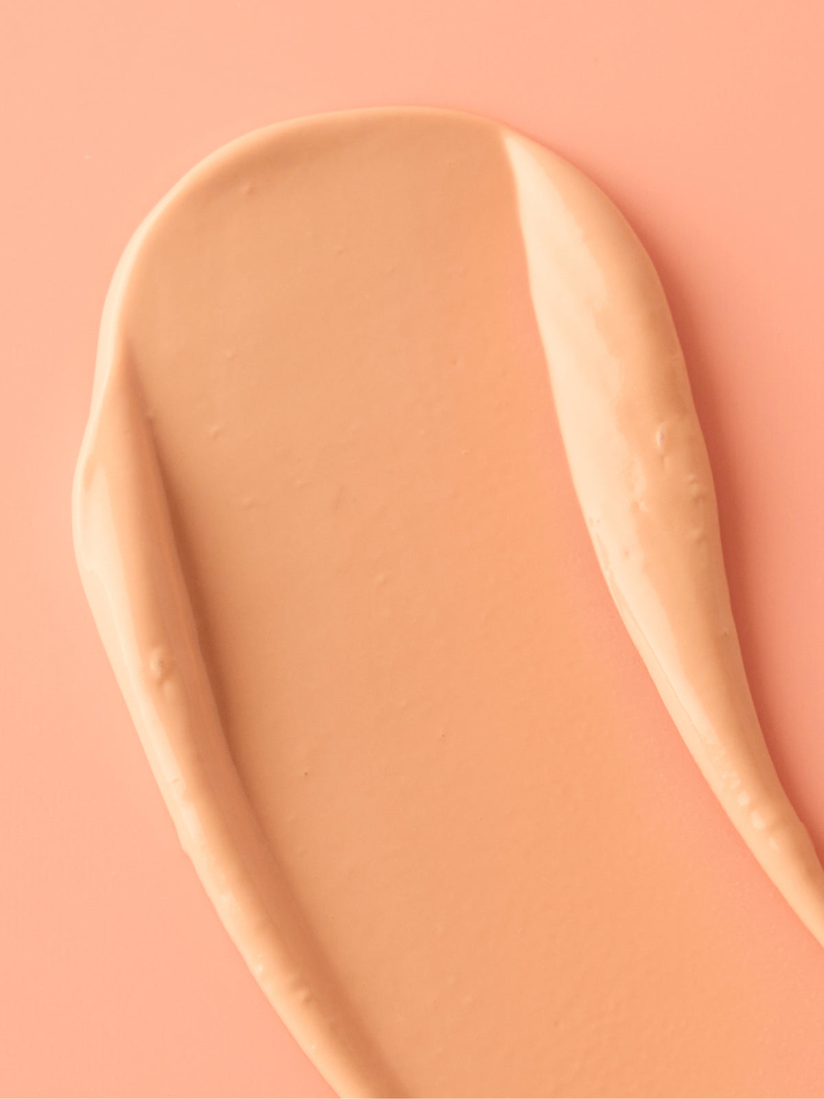Close up of a smooth peach colored sunscreen cream swatch on a coral background from Go To Skincare Nifty Gifty duo