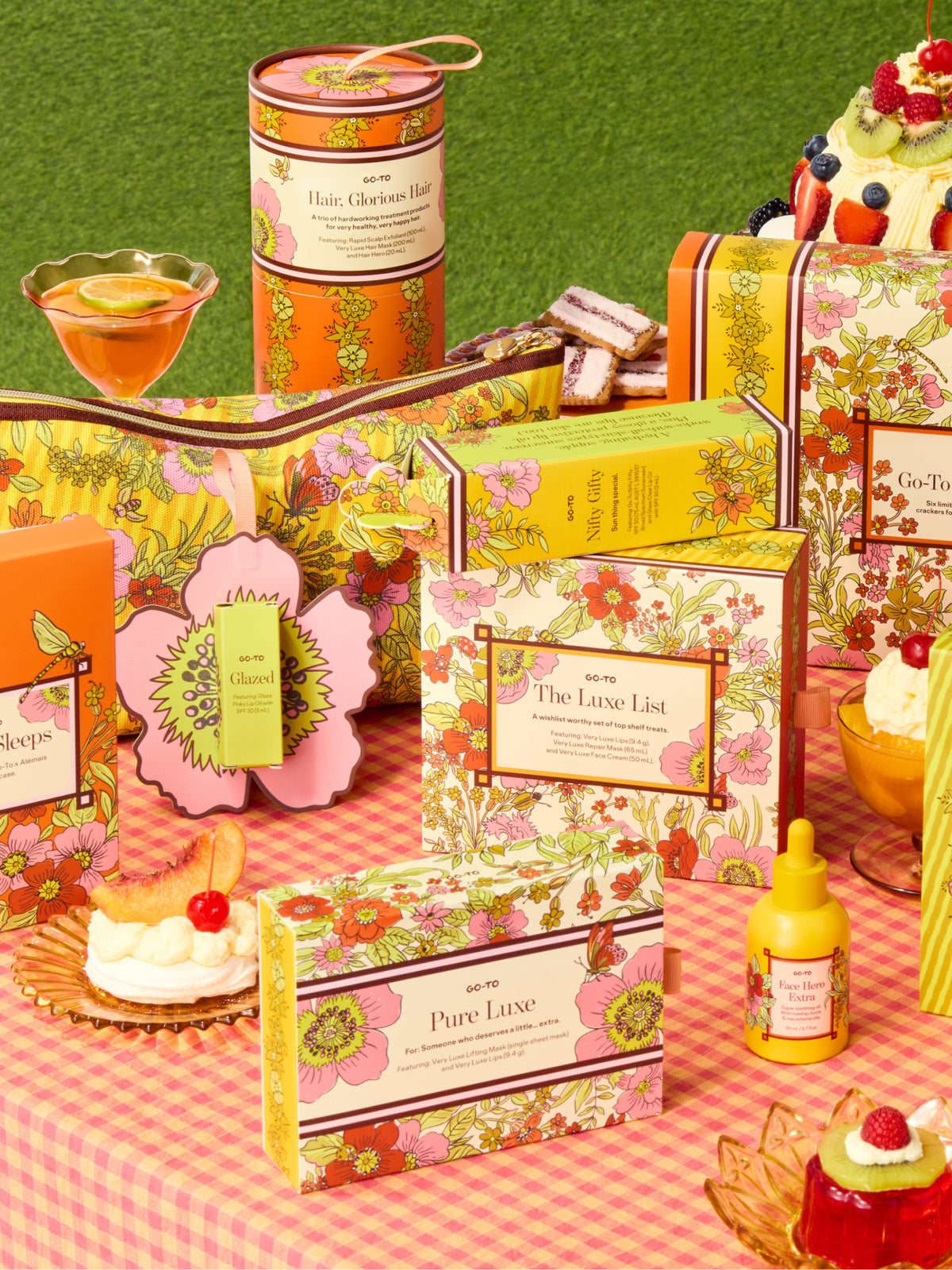 Pure Luxe floral skincare gift set by Go-To Skincare displayed with colorful patterned boxes and jars on a pink picnic table beside desserts and tea