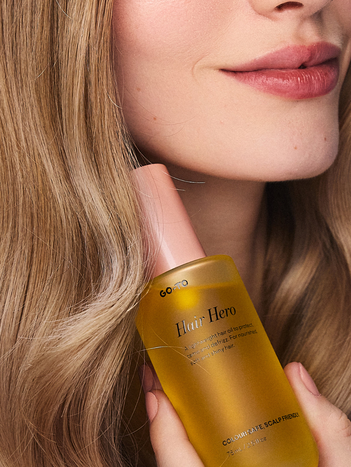Go To Hair Hero colour safe scalp serum bottle held beside a woman with long brown hair and natural rosy lips