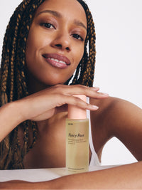 Smiling woman with braided hair holds a Go To Skincare cleansing bottle beside her face in a bright minimal skincare portrait