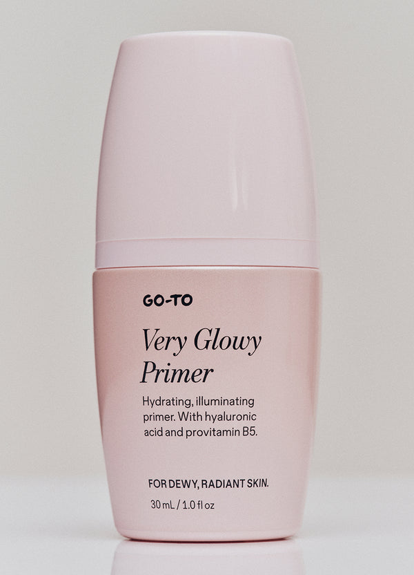 A pale pink bottle of Go-To Very Glowy Primer with black text describing it as a hydrating, illuminating primer with hyaluronic acid and provitamin B5, designed for dewy, radiant skin. 30 mL / 1.0 fl oz.
