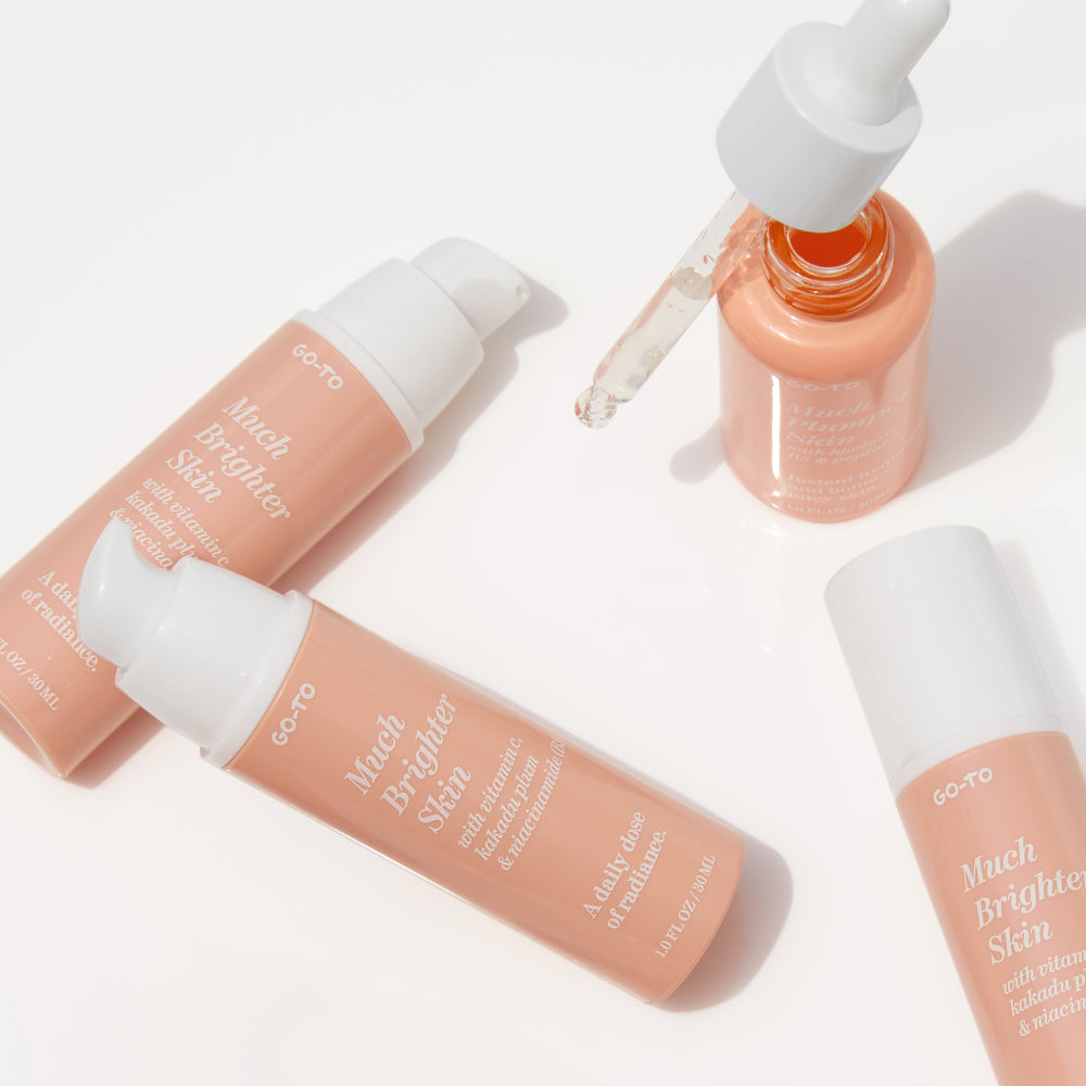 Four peach-colored skincare bottles labeled Much Brighter Skin and one matching dropper bottle with a pipette are arranged on a white surface in bright lighting.