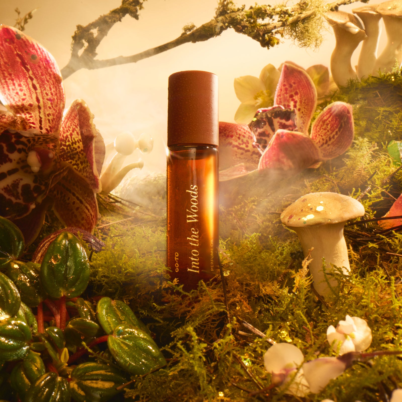 A perfume bottle labeled Into the Woods stands among moss, mushrooms, lush green leaves, and pink flowers, surrounded by soft, warm light and a misty, enchanted forest atmosphere.