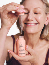 Smiling woman applies Go-To Much Plumper Skin serum with a dropper, highlighting skincare routine and product packaging.