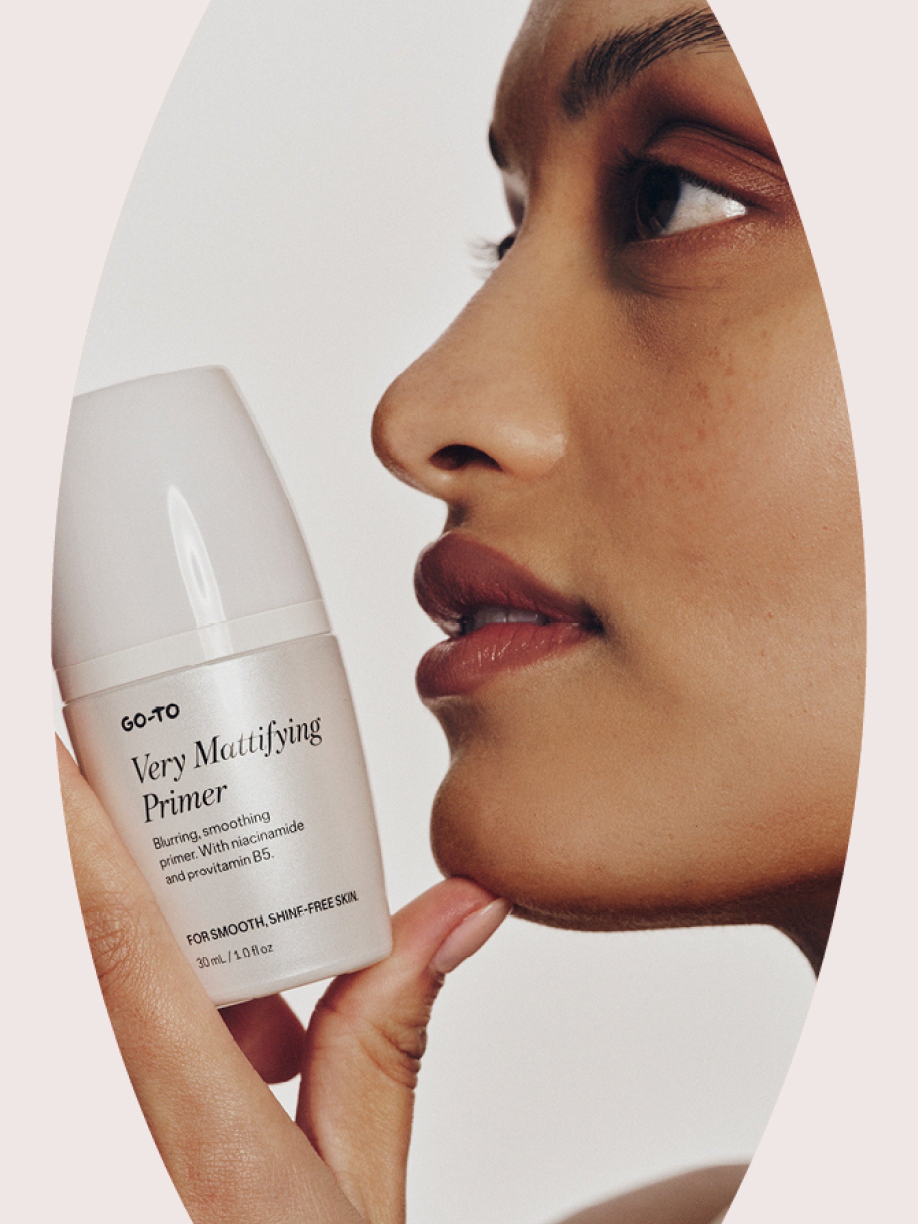 A person holds a bottle of Go-To Very Mattifying Primer close to their face, showcasing smooth, clear skin. The product label is visible, highlighting its benefits for shine-free skin.