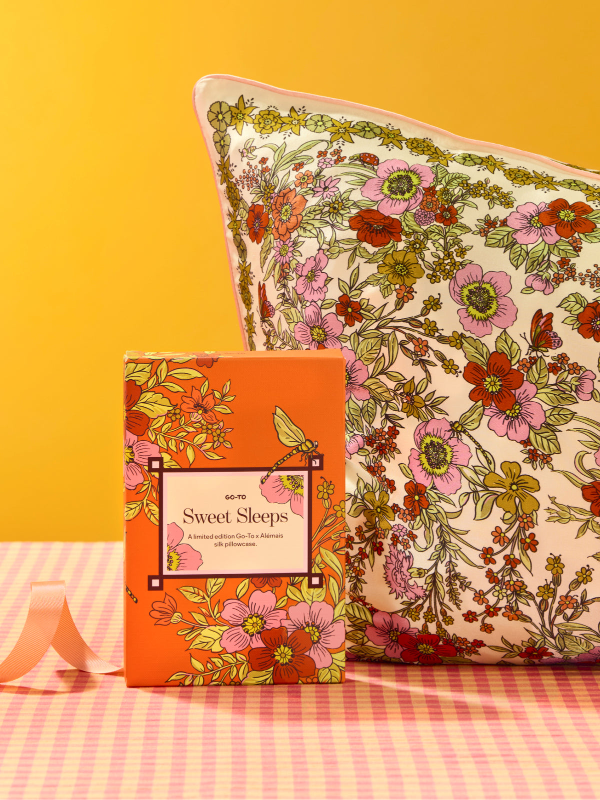 Floral Sweet Sleeps silk pillowcase and matching gift box displayed on a pink checkered surface against a bright orange background from Go To Skincare
