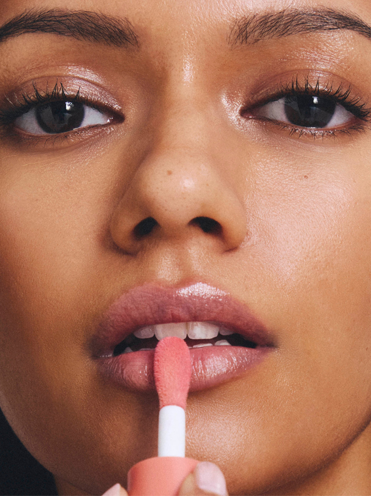 Close up of a model applying Go To Skincare Glazed tinted SPF lip oil with a pink applicator for glossy moisturized lips
