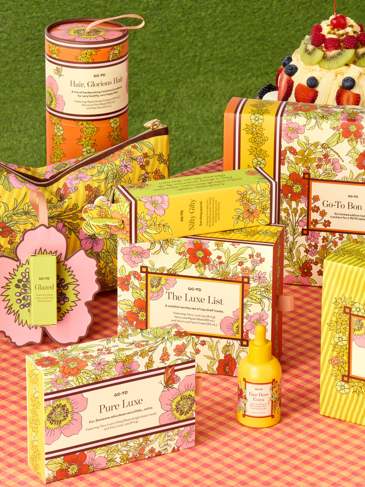 Go To Skincare Hair Glorious Hair gift set with colorful floral packaging arranged on a pink picnic cloth beside a festive fruit topped cake