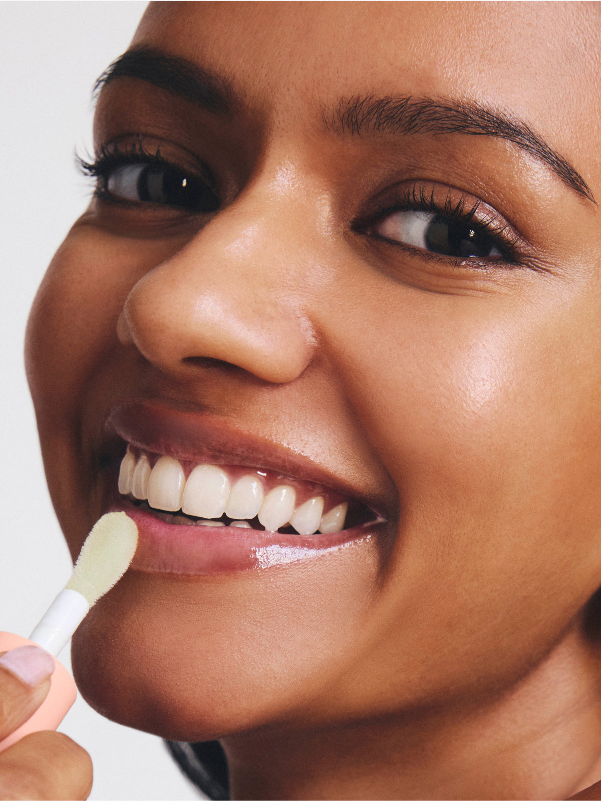 Close up of a smiling person applying a glossy skincare product to the lips with a small applicator from Go To Skincare