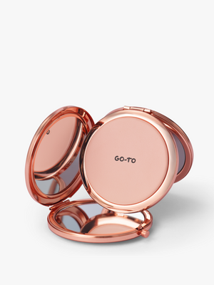 Rose gold compact mirror opened to reveal reflective mirror surfaces and a blush pink round panel marked Go To on a white background from Go To Skincare